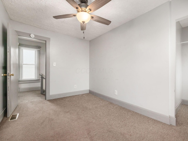 empty room with baseboards, visible vents, ceiling fan, a textured ceiling, and carpet floors