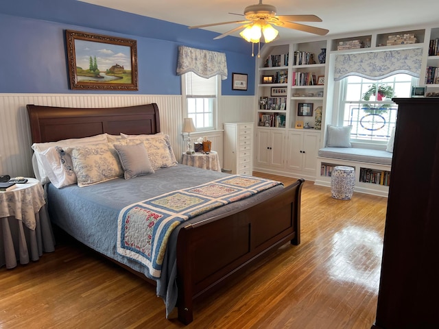 bedroom with a wainscoted wall, wood finished floors, and a ceiling fan