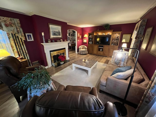 living area with arched walkways, a fireplace with flush hearth, crown molding, and wood finished floors