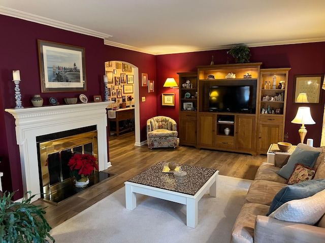 living area featuring arched walkways, a fireplace with flush hearth, ornamental molding, and wood finished floors