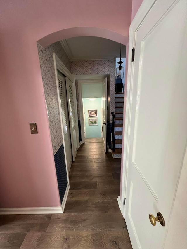 corridor with arched walkways, wallpapered walls, baseboards, and wood finished floors