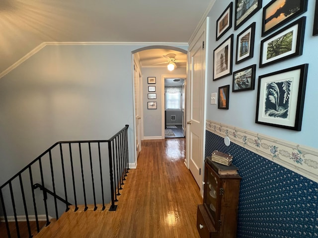 corridor with wood finished floors, baseboards, arched walkways, crown molding, and an upstairs landing