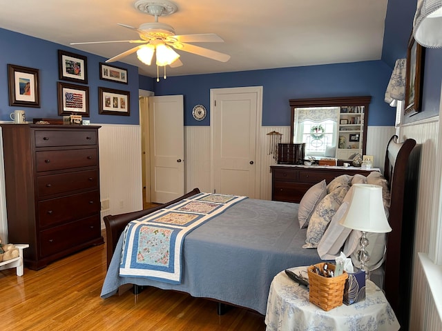 bedroom featuring a wainscoted wall, a ceiling fan, and wood finished floors