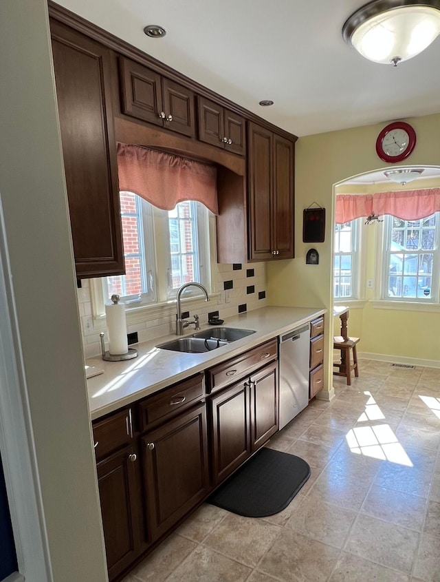 kitchen with a sink, light countertops, dark brown cabinets, stainless steel dishwasher, and tasteful backsplash