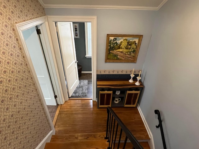 hall featuring wallpapered walls, wood finished floors, baseboards, and ornamental molding