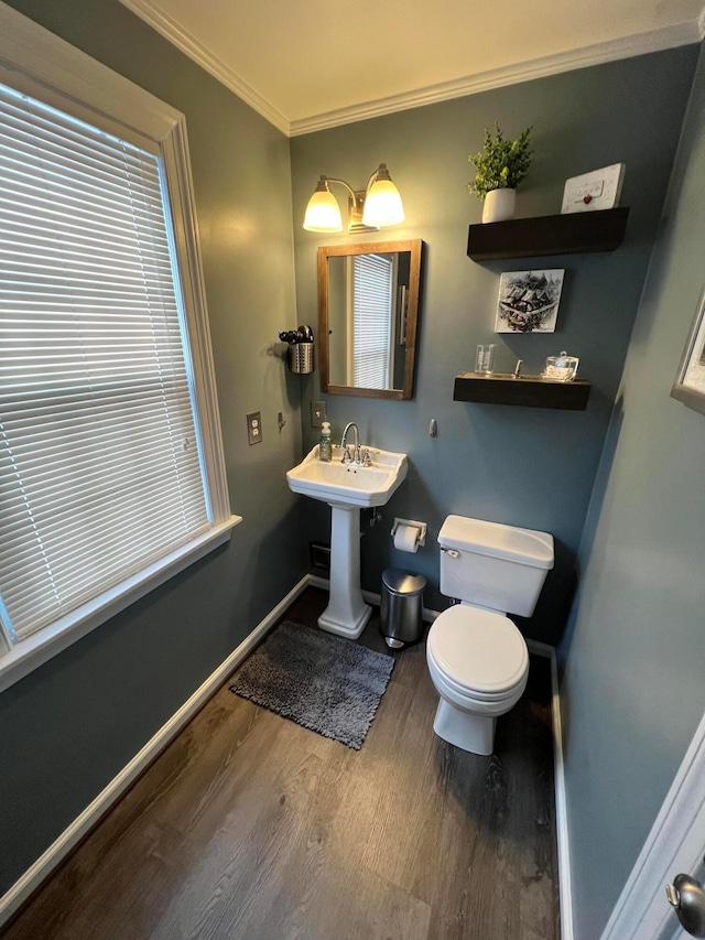 half bath with baseboards, toilet, ornamental molding, wood finished floors, and a sink