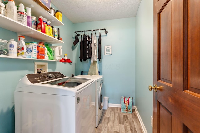 washroom featuring a textured ceiling, light wood-style flooring, laundry area, baseboards, and washer and clothes dryer