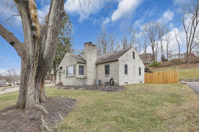 exterior space featuring central AC unit, fence, a yard, stone siding, and a chimney