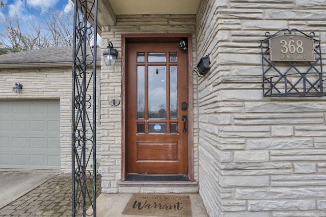 doorway to property with a garage, stone siding, and roof with shingles