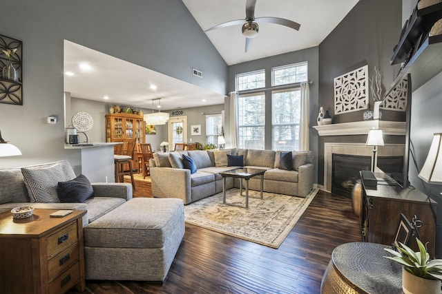 living area featuring ceiling fan, high vaulted ceiling, visible vents, dark wood-style floors, and a tiled fireplace