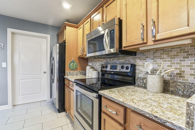 kitchen featuring light stone countertops, stainless steel appliances, baseboards, decorative backsplash, and brown cabinets