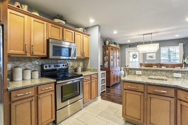 kitchen with stainless steel appliances, brown cabinetry, backsplash, and light stone countertops