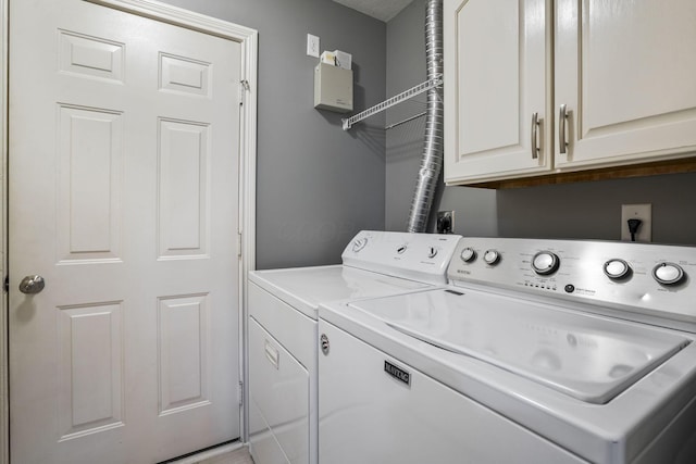 clothes washing area with separate washer and dryer and cabinet space