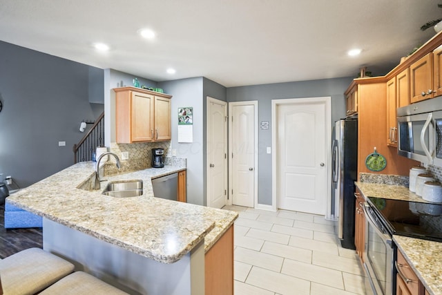 kitchen featuring stainless steel appliances, a peninsula, a sink, a kitchen breakfast bar, and light stone countertops