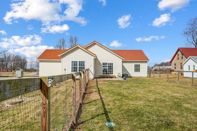 rear view of house featuring metal roof, a lawn, and a fenced backyard