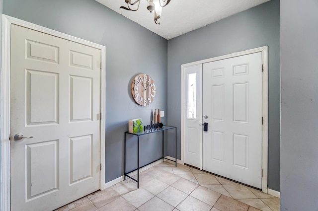 foyer entrance with light tile patterned flooring, baseboards, and an inviting chandelier