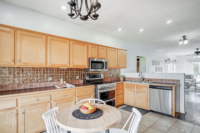 kitchen with stainless steel appliances, a sink, backsplash, and light brown cabinetry