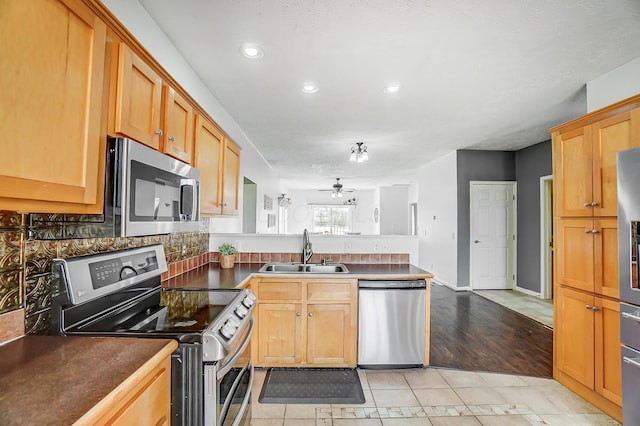 kitchen with a peninsula, dark countertops, stainless steel appliances, and a sink