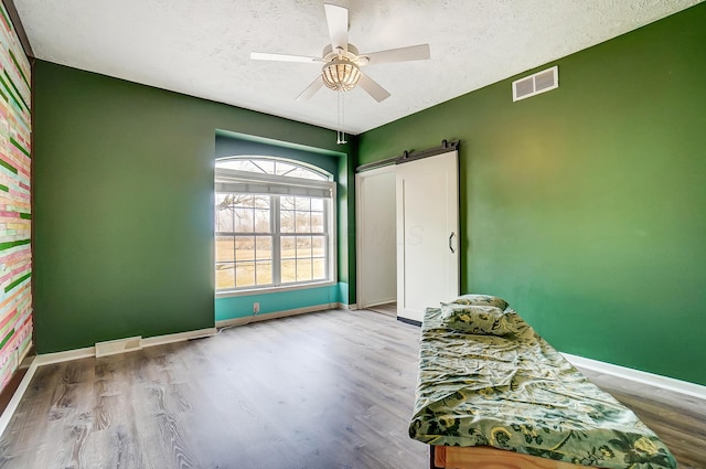 unfurnished room featuring a barn door, wood finished floors, visible vents, and baseboards