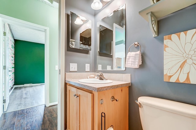 bathroom with toilet, wood finished floors, vanity, and baseboards