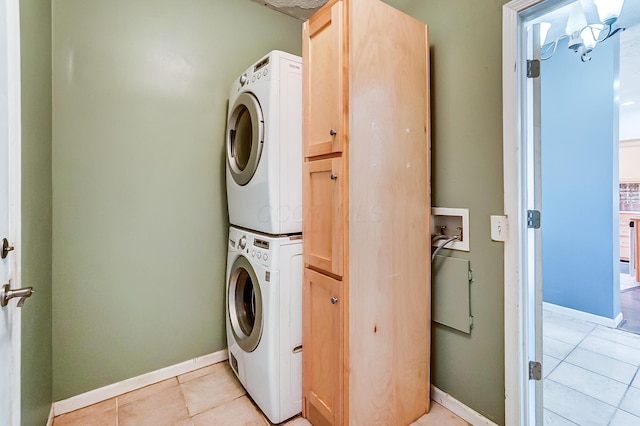 laundry area featuring stacked washer and clothes dryer, cabinet space, baseboards, and light tile patterned floors