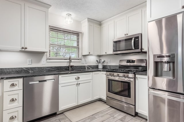 kitchen with wood finish floors, appliances with stainless steel finishes, white cabinetry, a sink, and a textured ceiling