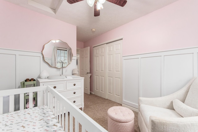 bedroom with light colored carpet, a wainscoted wall, a nursery area, a decorative wall, and a closet