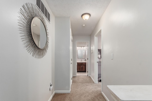 hall with baseboards, visible vents, a textured ceiling, and light colored carpet