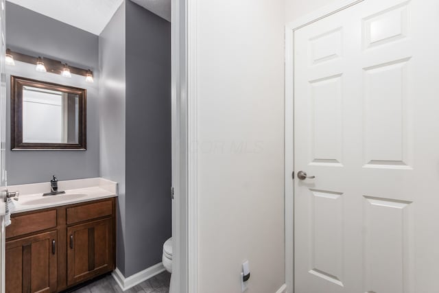 bathroom featuring toilet, baseboards, and vanity