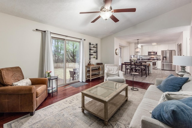 living area featuring vaulted ceiling, light wood finished floors, a textured ceiling, and a ceiling fan