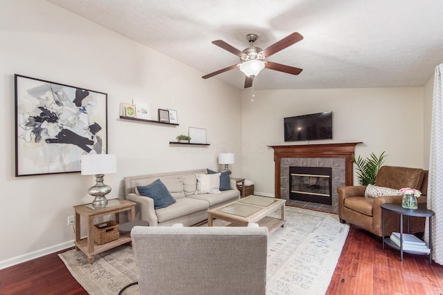 living room with a tile fireplace, wood finished floors, a ceiling fan, baseboards, and vaulted ceiling