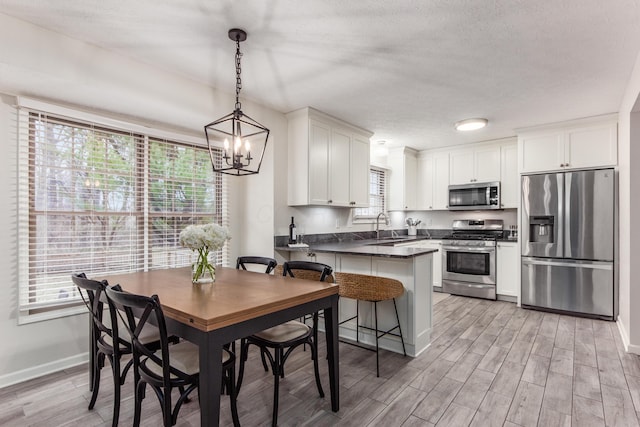 kitchen featuring stainless steel appliances, a peninsula, a sink, light wood-style floors, and dark countertops