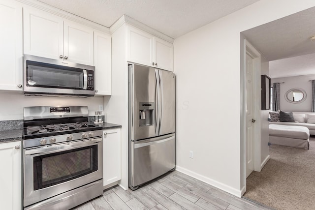 kitchen with white cabinetry, baseboards, light wood-style floors, appliances with stainless steel finishes, and dark countertops