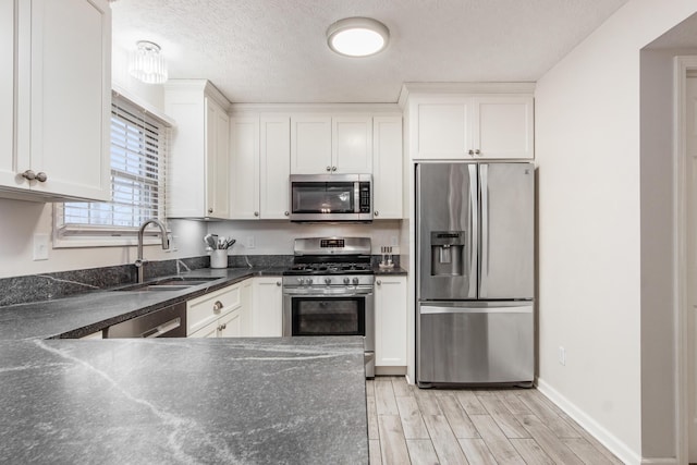 kitchen with a textured ceiling, wood finish floors, a sink, white cabinets, and appliances with stainless steel finishes