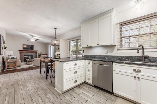 kitchen with a tile fireplace, a peninsula, wood finish floors, stainless steel dishwasher, and a sink