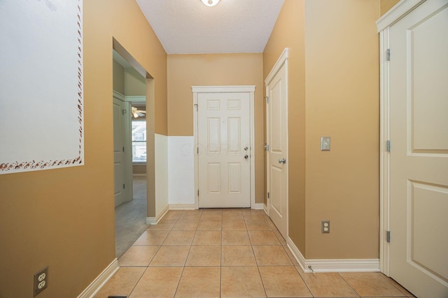 hall with light tile patterned floors, baseboards, and a textured ceiling