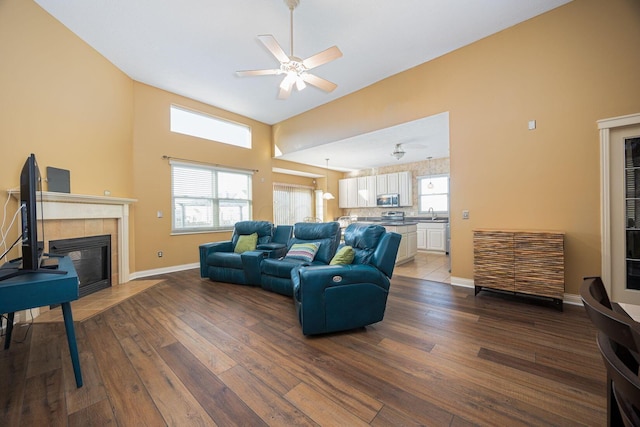 living room featuring dark wood finished floors, ceiling fan, a tiled fireplace, and baseboards