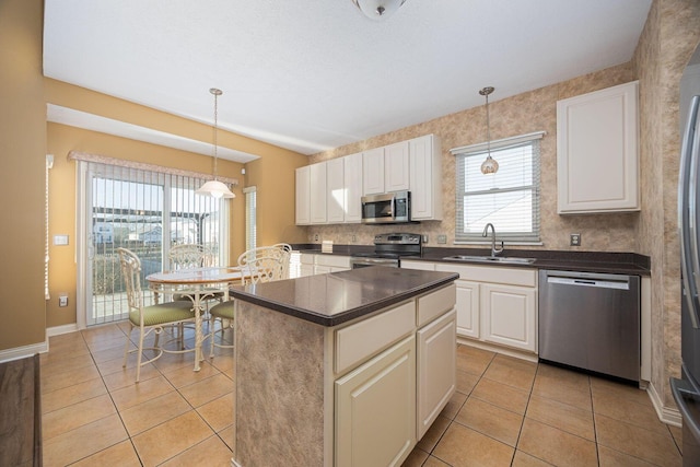 kitchen with a sink, a kitchen island, dark countertops, appliances with stainless steel finishes, and light tile patterned floors