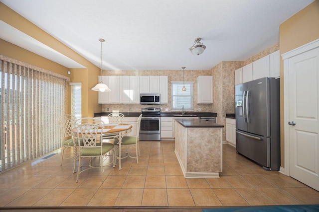 kitchen with a sink, a kitchen island, stainless steel appliances, white cabinets, and light tile patterned floors