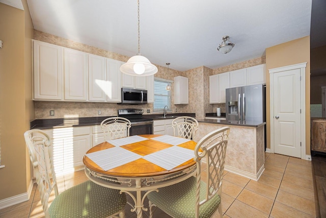 kitchen featuring dark countertops, appliances with stainless steel finishes, light tile patterned flooring, white cabinets, and a sink