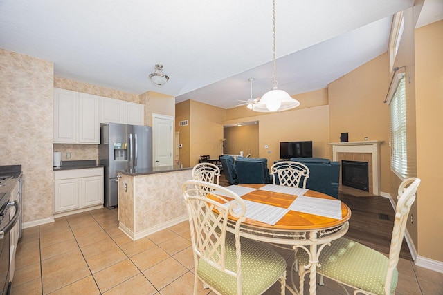 dining space featuring light tile patterned floors, a fireplace, baseboards, and ceiling fan