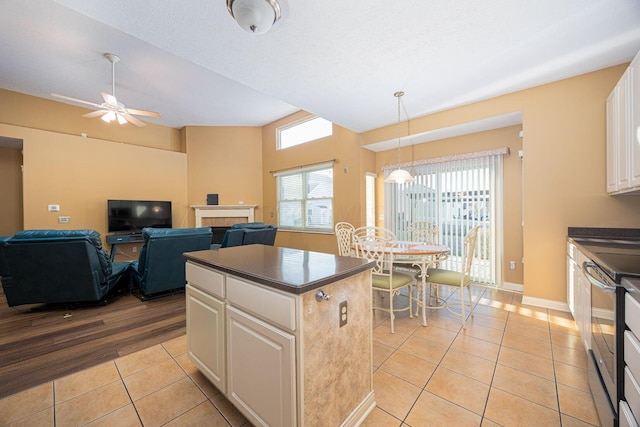 kitchen with light tile patterned floors, a kitchen island, electric stove, a tiled fireplace, and dark countertops