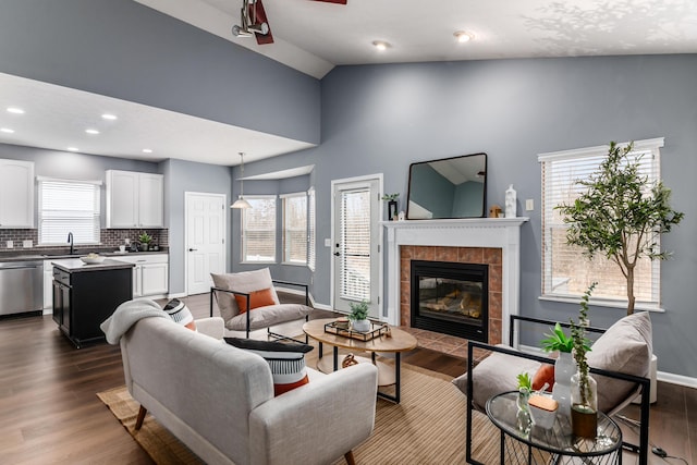 living area with a wealth of natural light, a fireplace, vaulted ceiling, and dark wood-style flooring