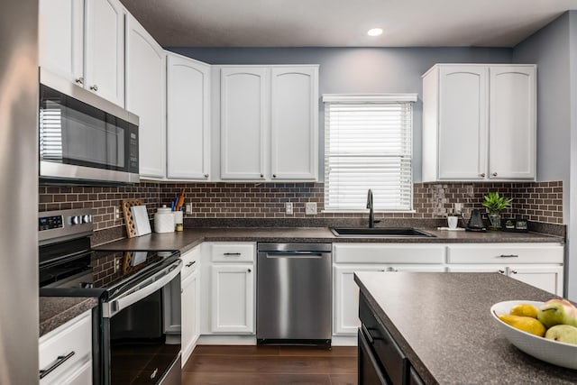 kitchen with dark wood-style floors, stainless steel appliances, dark countertops, white cabinets, and a sink