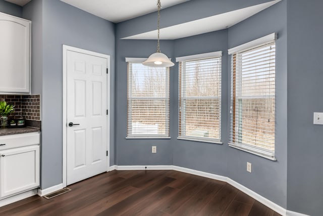 unfurnished dining area with baseboards, visible vents, and dark wood-style flooring