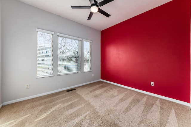 carpeted spare room featuring an accent wall, visible vents, ceiling fan, and baseboards