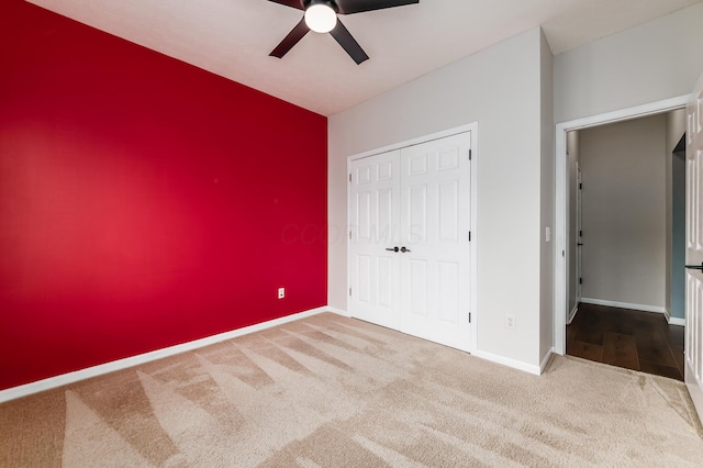 unfurnished bedroom with carpet floors, a closet, an accent wall, a ceiling fan, and baseboards