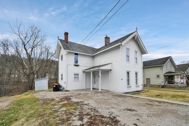 view of front of home featuring a shingled roof, driveway, a chimney, and a front lawn