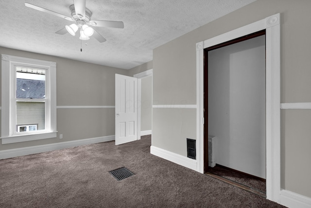 spare room featuring a textured ceiling, dark carpet, visible vents, and baseboards