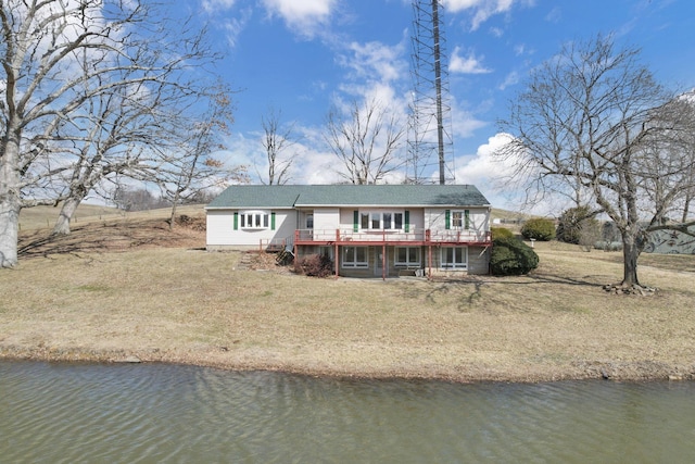 rear view of house with a deck with water view and a lawn